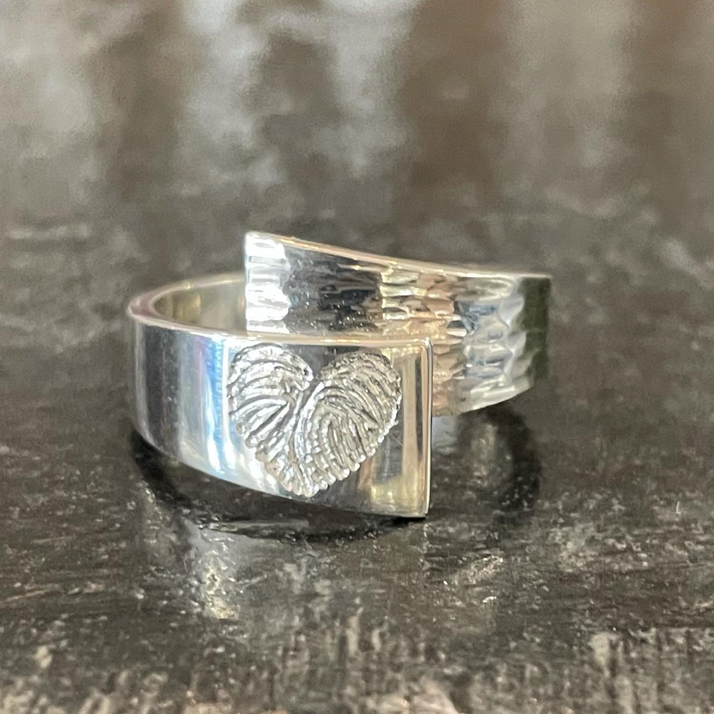 Zilveren ring met een vingerafdrukafdruk in de vorm van een hart.
