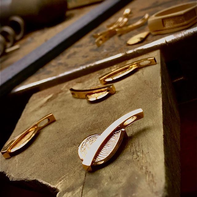 Gouden sieraden op een houten werkblad, naast gereedschap.
