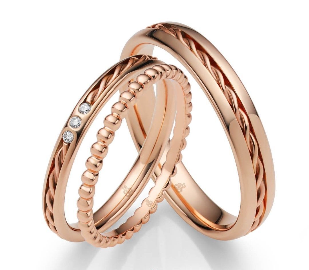 Drie trouwringen van roségoud, waarvan één met drie kleine diamanten, alle drie met gevlochten of geparelde details.