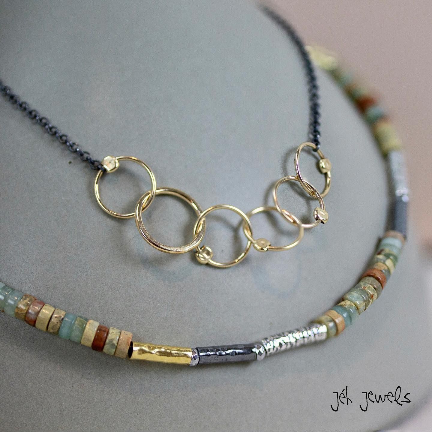 Twee kettingen: goudkleurige, aaneengeschakelde cirkels op een zwarte ketting, turquoise/bruine kralenstreng.