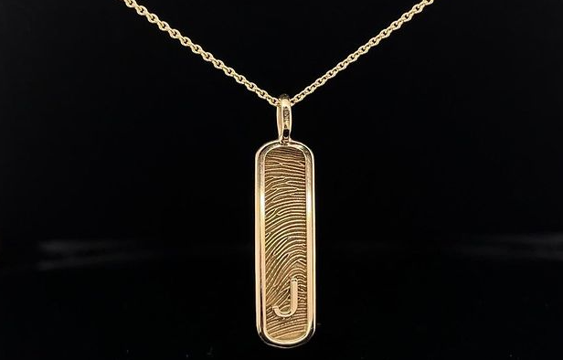 Gouden ketting met een hanger met een vingerafdrukontwerp en de letter 