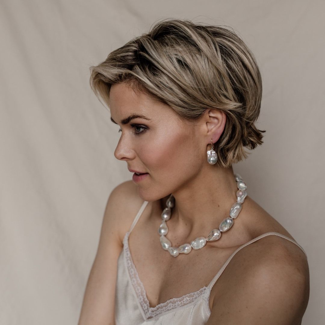 Vrouw met kort blond haar, parelketting en oorbellen, kijkend naar links.
