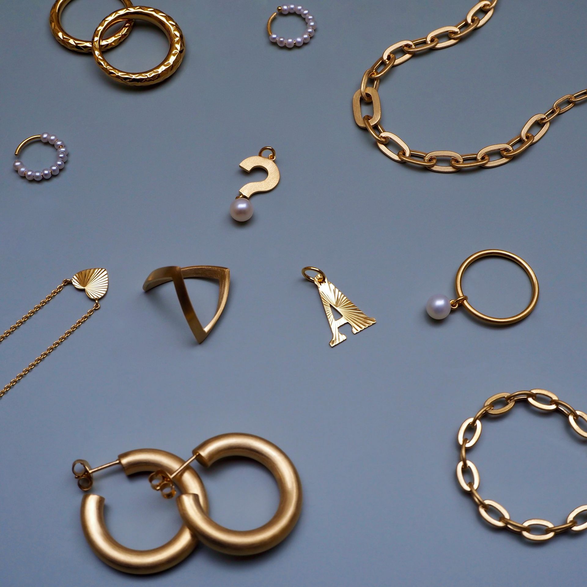Gouden sieraden op een grijze ondergrond: ringen, kettingen, oorbellen en bedels.