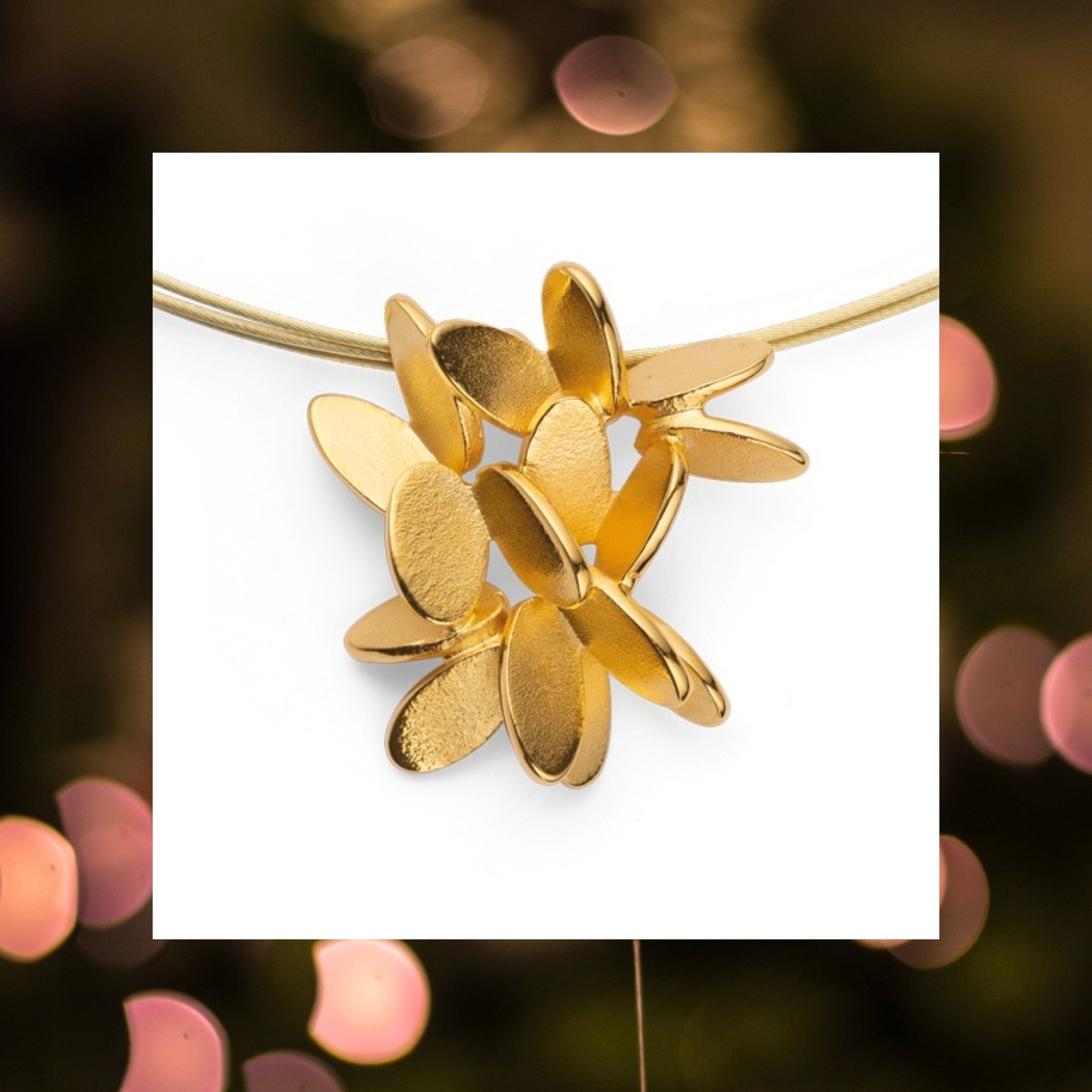 Ketting met gouden bloemenhanger aan een gouden ketting, afstekend tegen wazig licht.