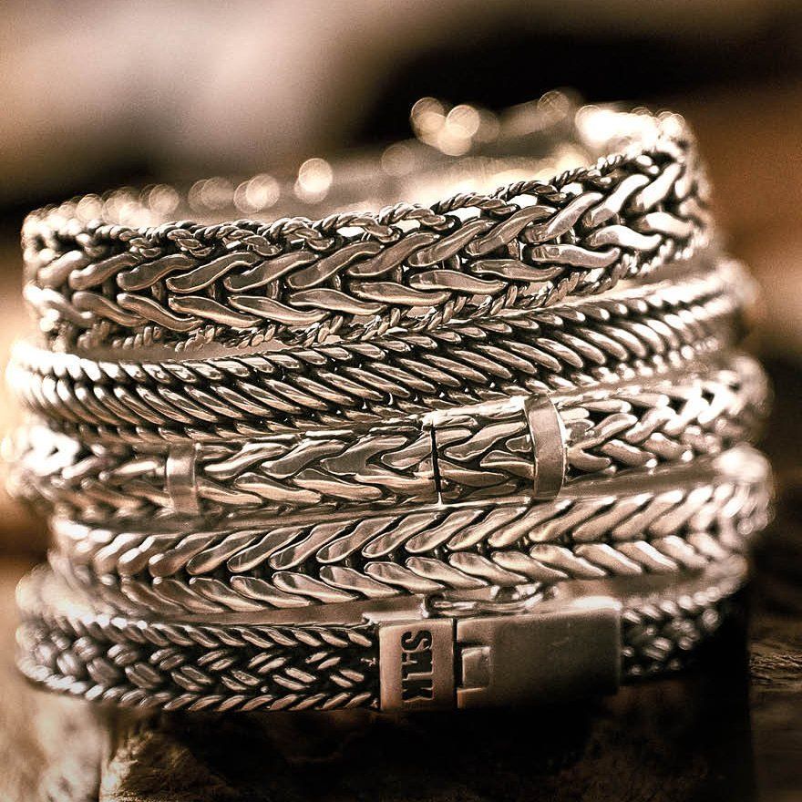 Close-up van een stapel gevlochten zilveren armbanden met verschillende ingewikkelde ontwerpen.