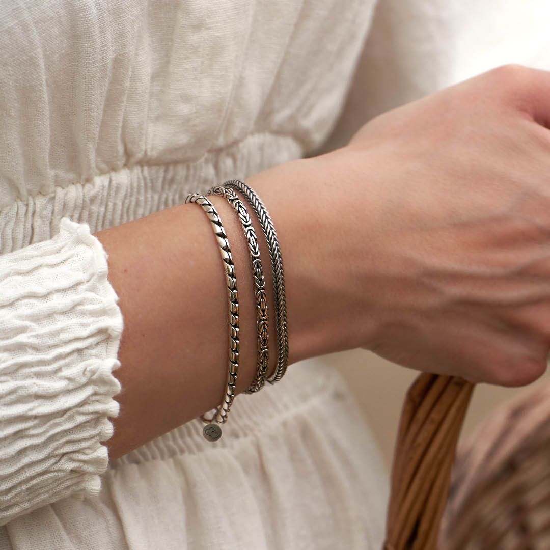 Drie zilveren armbanden om een pols, naast een witte mouw.