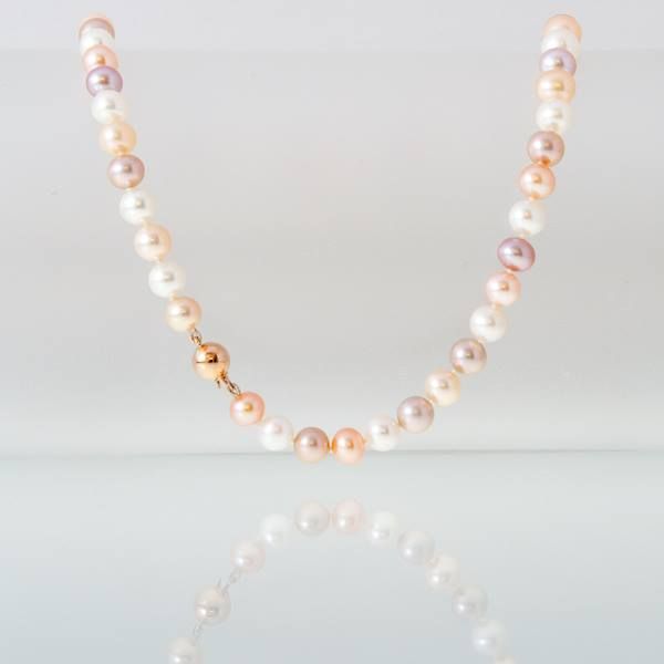 Parelketting met witte, roze en perzikkleurige kralen en een gouden sluiting, rustend op een reflecterend oppervlak.