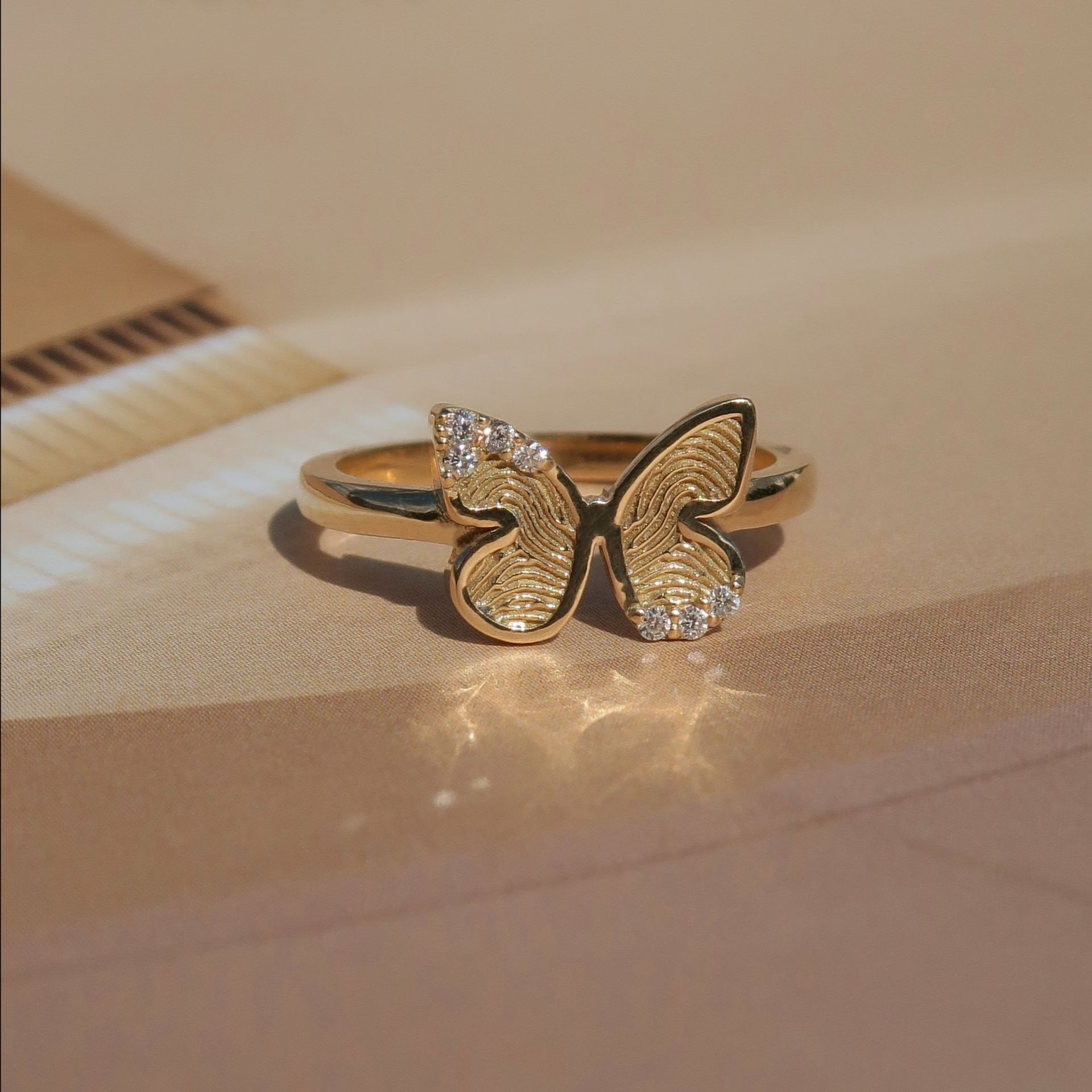 Gouden vlinderring met getextureerde vleugels, kleine diamanten en een zachte achtergrond.