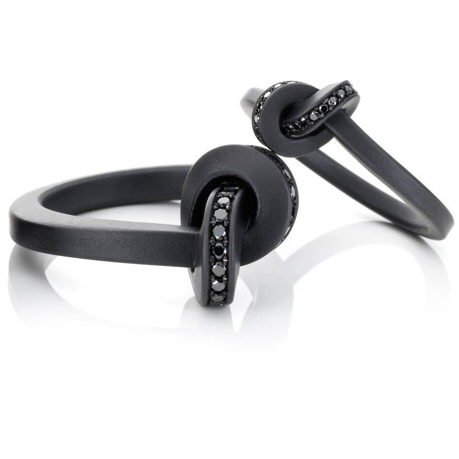 Twee donkere ringen met zwarte edelstenen in een knoopmotief, op een witte achtergrond.