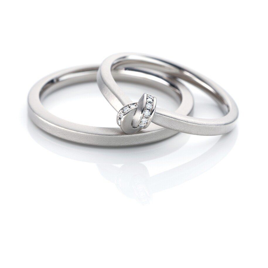 Twee zilveren trouwringen, waarvan één met een knoopmotief en kleine diamanten.