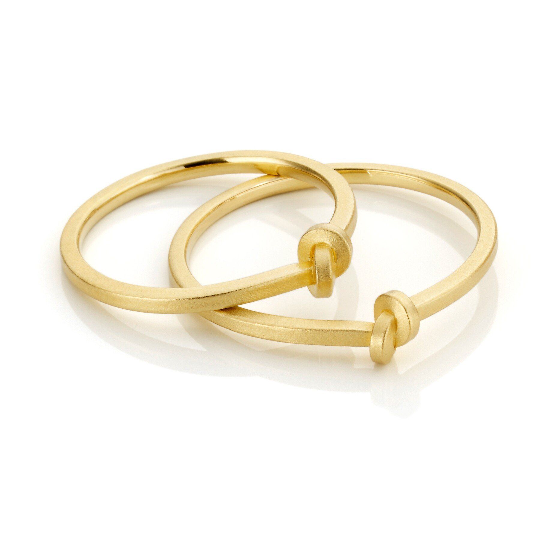 Twee goudkleurige armbanden met knoopdetails, overlappen elkaar op een wit oppervlak.