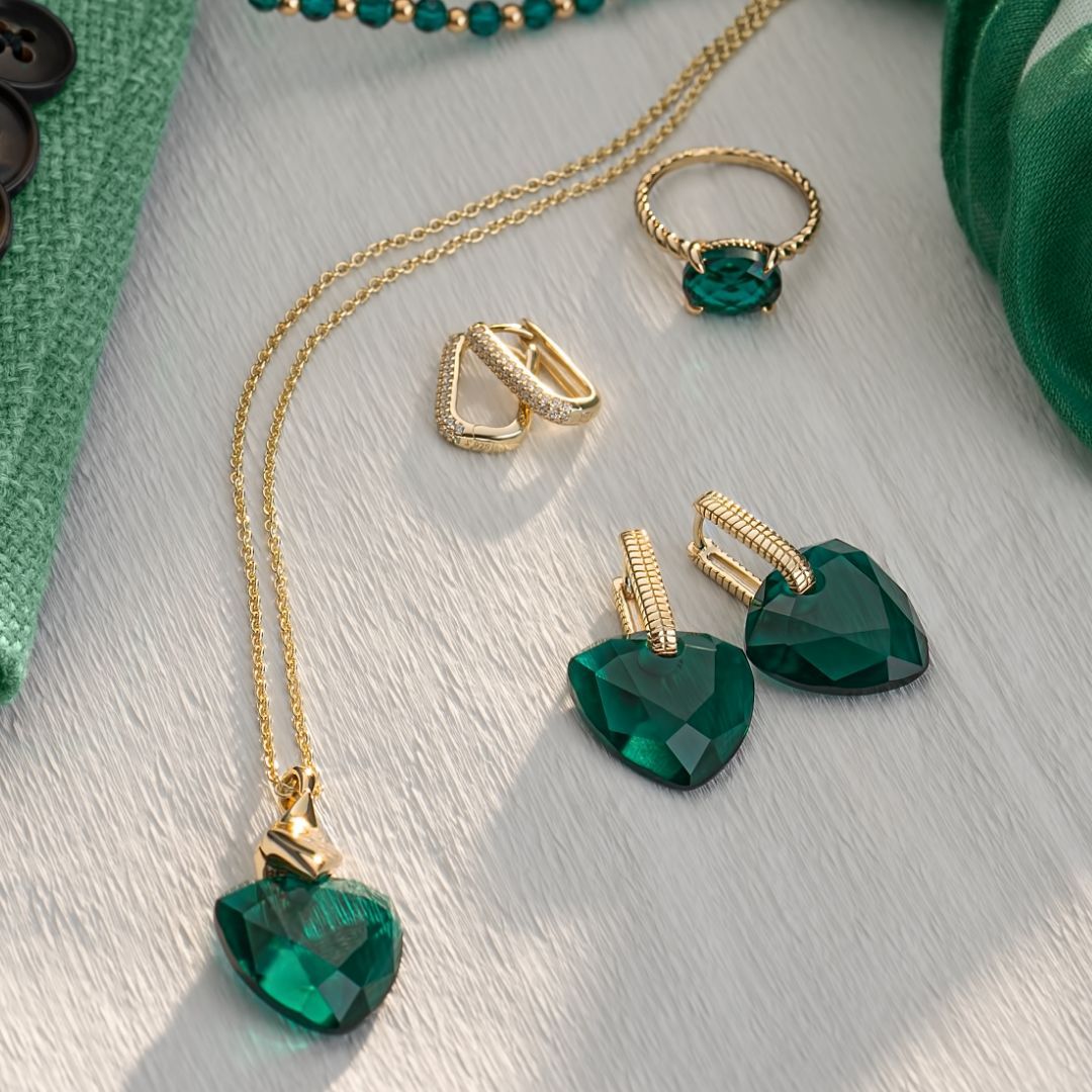 Gouden sieradenset met smaragdgroene harthanger ketting, oorbellen, ring en kralenarmband.