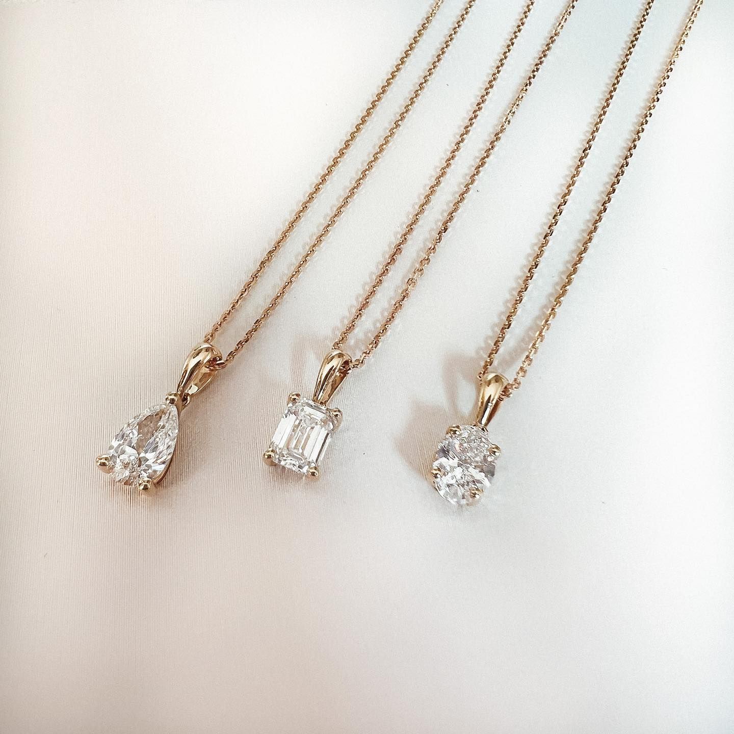 Drie gouden kettingen met diamanten hangers: peer-, smaragd- en ovaalgeslepen.