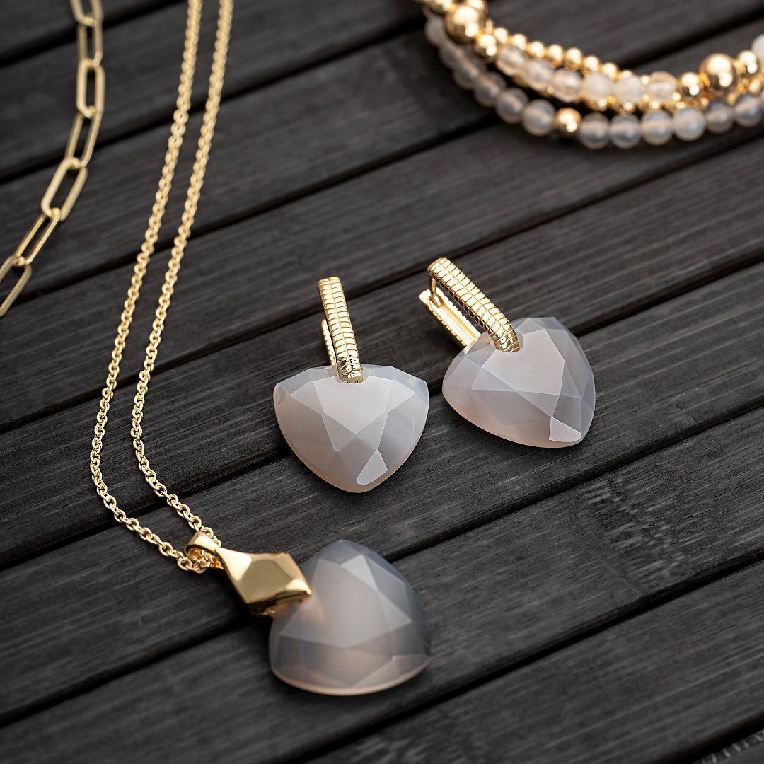 Gouden ketting met hartvormige hanger, bijpassende oorbellen en kralenarmbanden op een donker houten oppervlak.