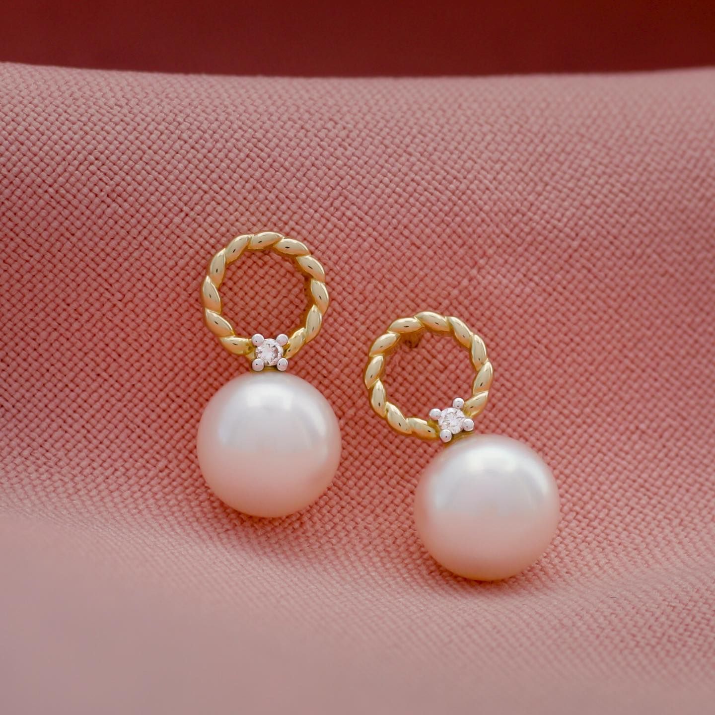 Pareloorbellen op roze stof. Gouden ringen met diamanten boven witte parels.