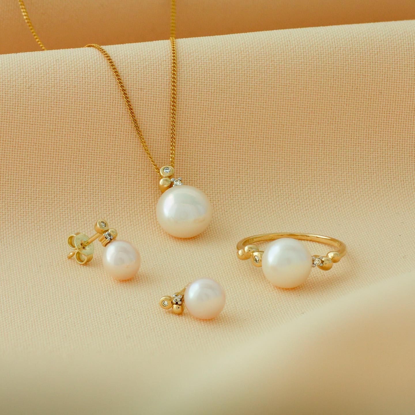 Gouden sieradenset met parels: ketting, oorbellen en ring op lichtgele stof.