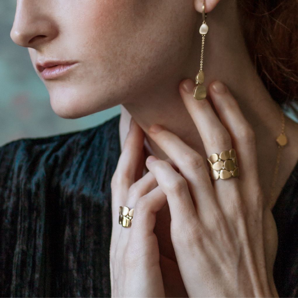 Vrouw met gouden sieraden: oorbellen, ringen. Groen topje, hand om haar nek.