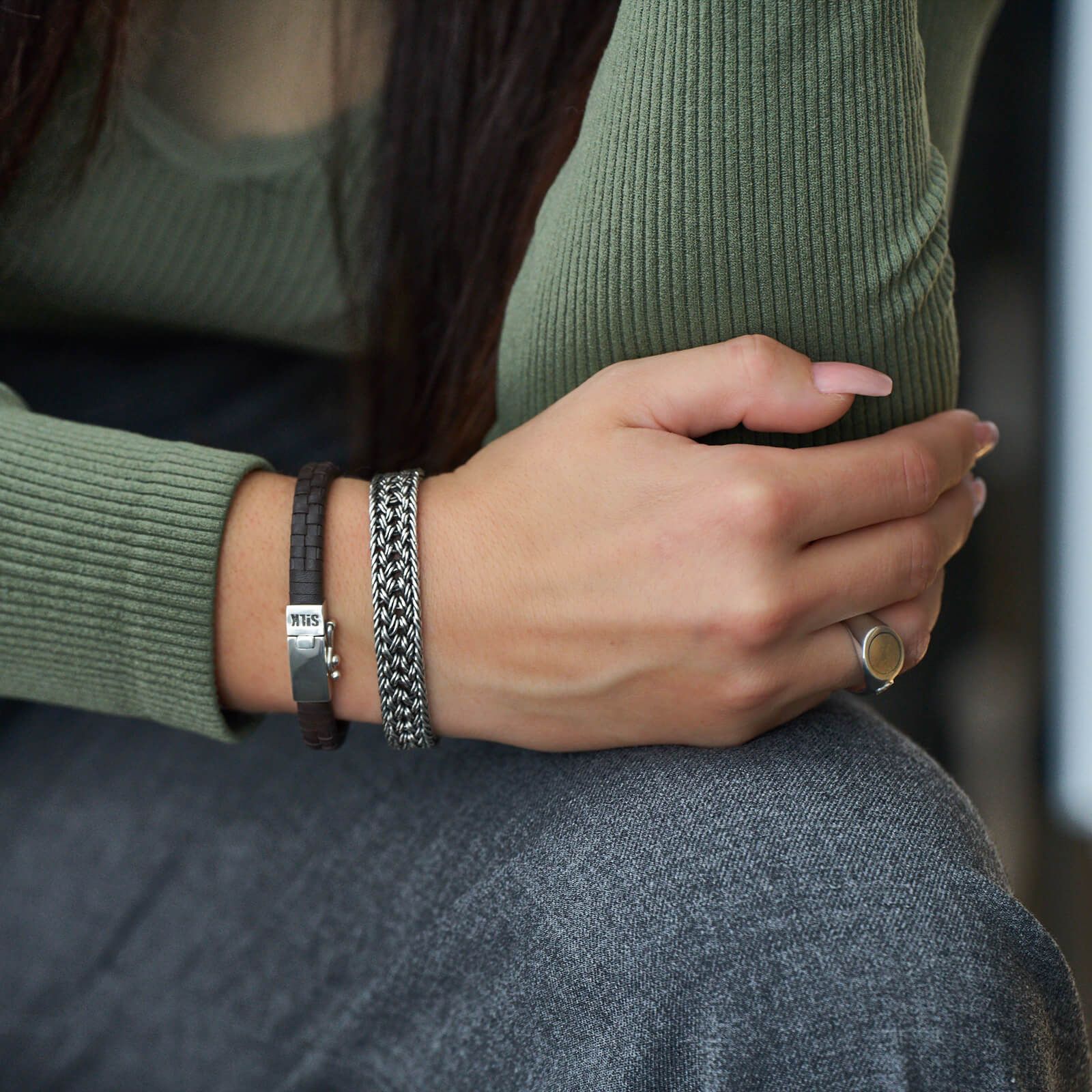 Vrouw draagt een groen shirt en een grijze spijkerbroek met twee armbanden en een ring.