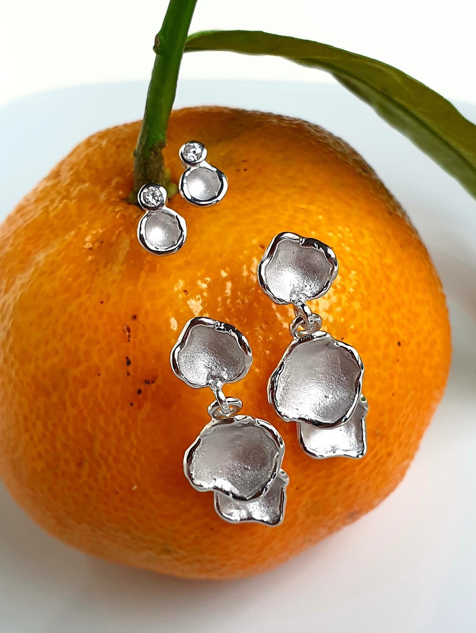 Zilveren oorbellen in de vorm van een blad, versierd met een feloranje mandarijn met een groene steel en blad.