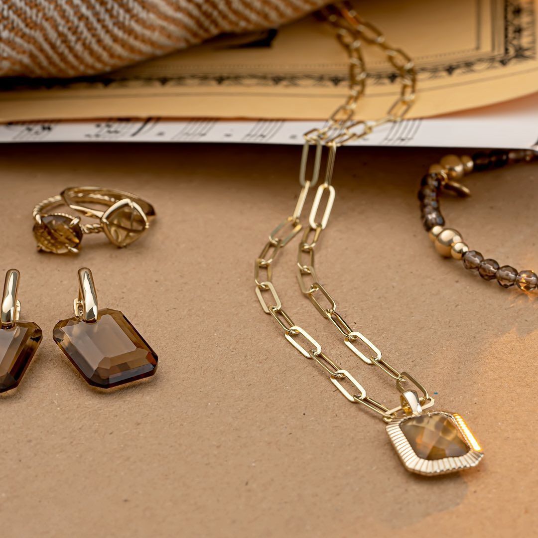 Sieradenset op bruin oppervlak: gouden ketting, oorbellen, ring en armband met accenten van bruine edelstenen.
