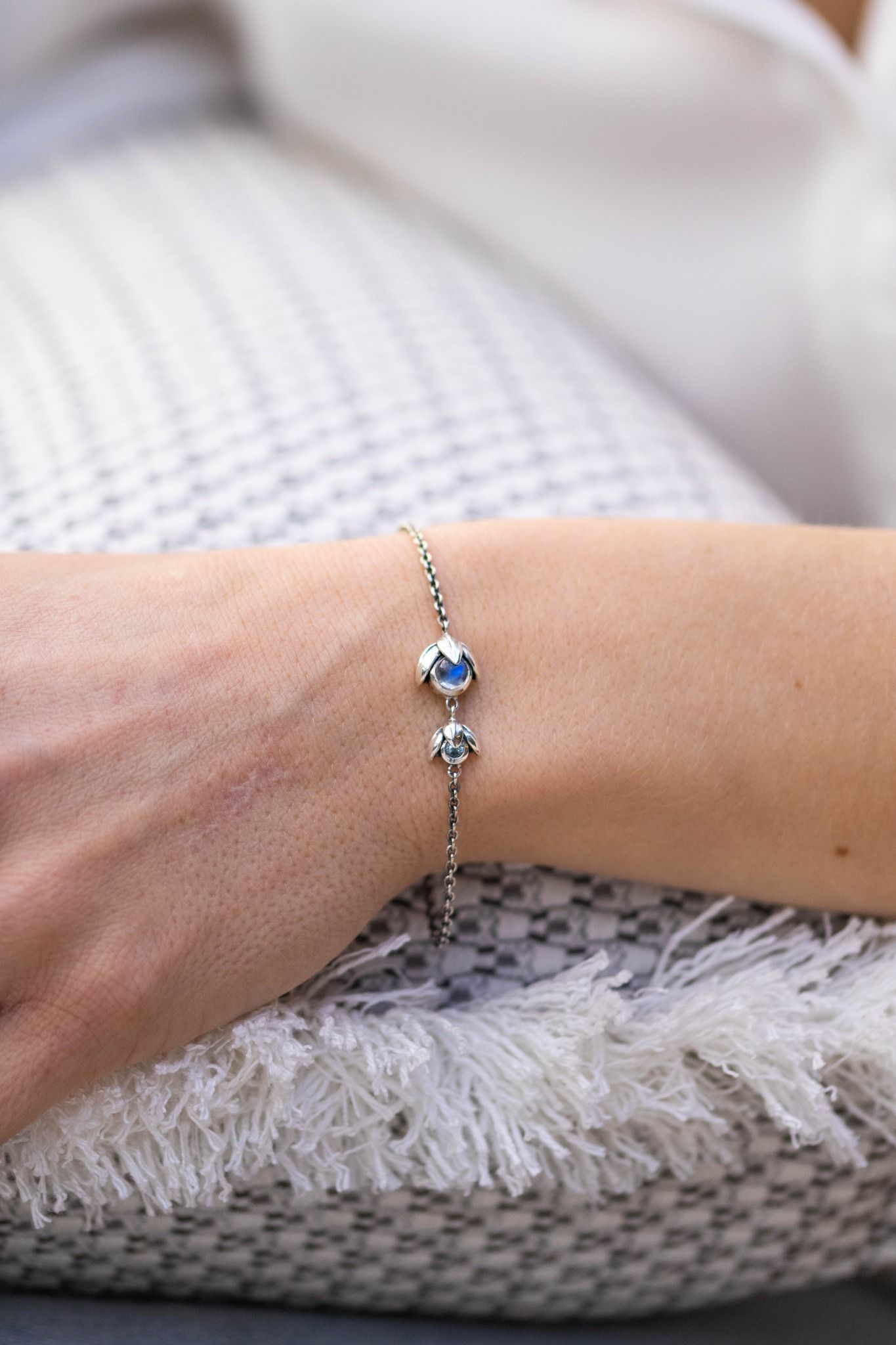 Zilveren armband met twee blauwe edelstenen om de pols, rustend op een kussen met structuur.