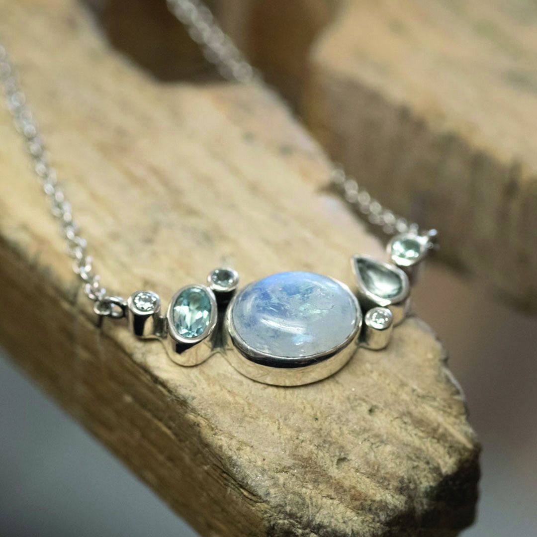 Zilveren ketting met maansteen en blauwe edelstenen op een houten oppervlak.