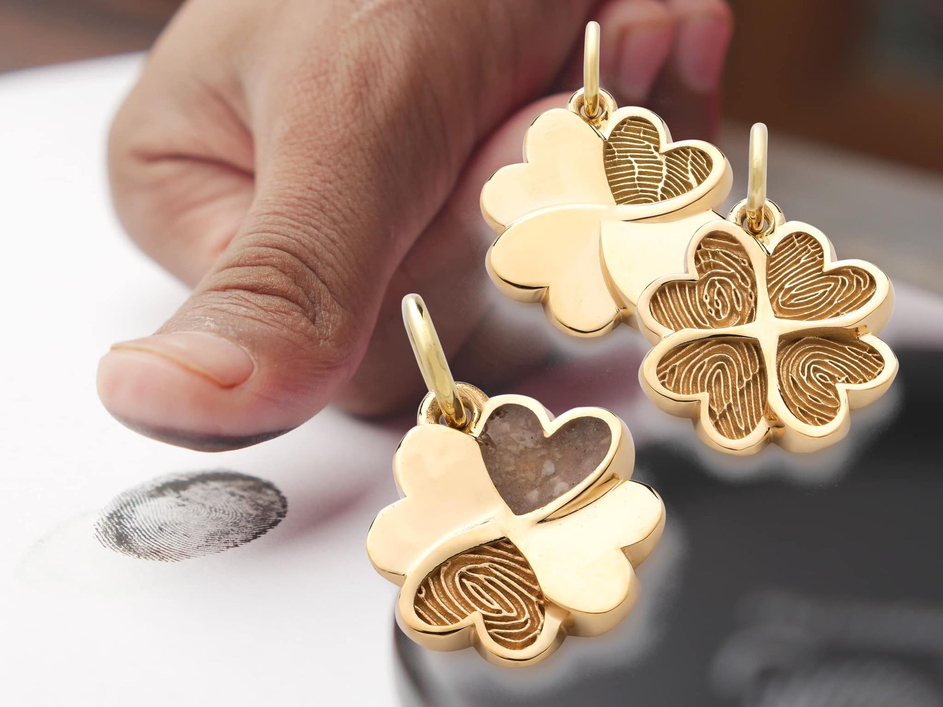 Gouden klavertjeshangers met vingerafdrukafdrukken, naast een vinger die een vingerafdruk neemt.