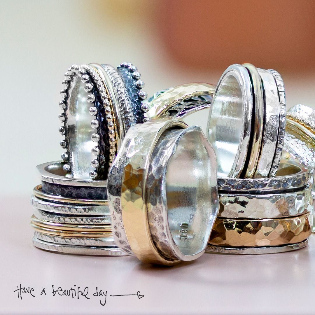 Stapel zilveren ringen met gouden accenten; zachte focus, roze achtergrond.