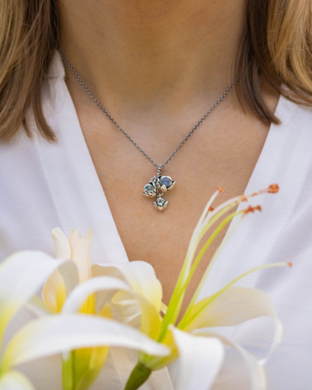 Vrouw draagt een zilveren hanger en houdt een witte bloem vast.