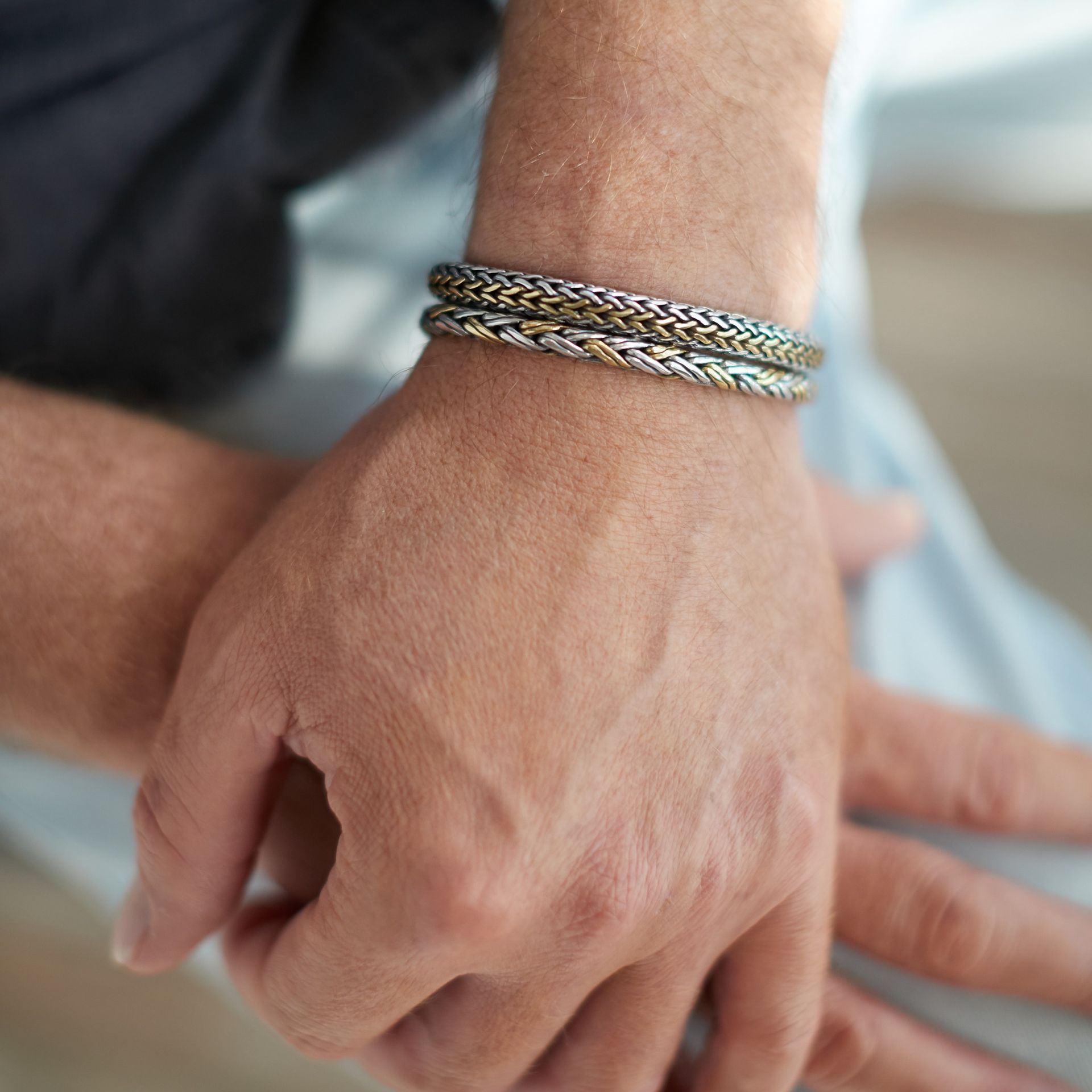 Close-up van de pols van een persoon met twee gevlochten metalen armbanden.