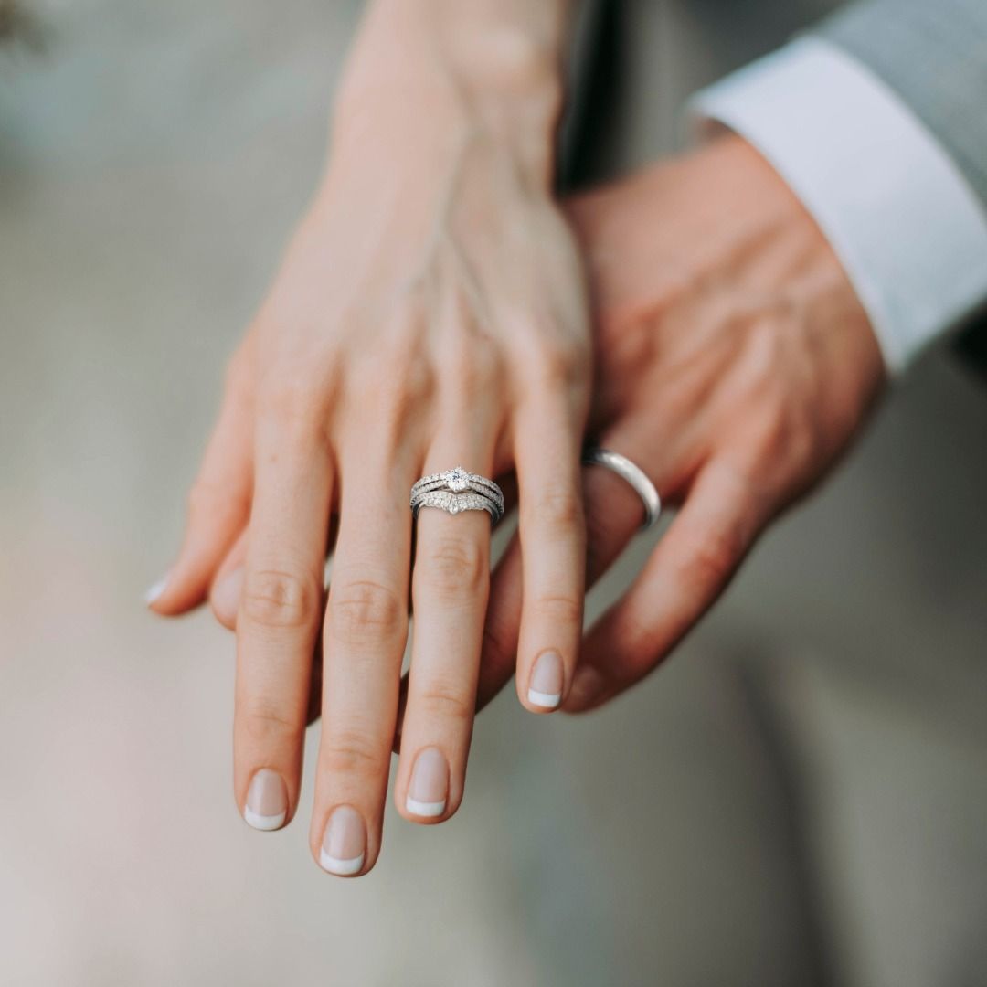 Close-up van twee handen die elkaar vasthouden. Eén hand heeft een diamanten ring aan de ringvinger. De andere hand heeft een zilveren band.