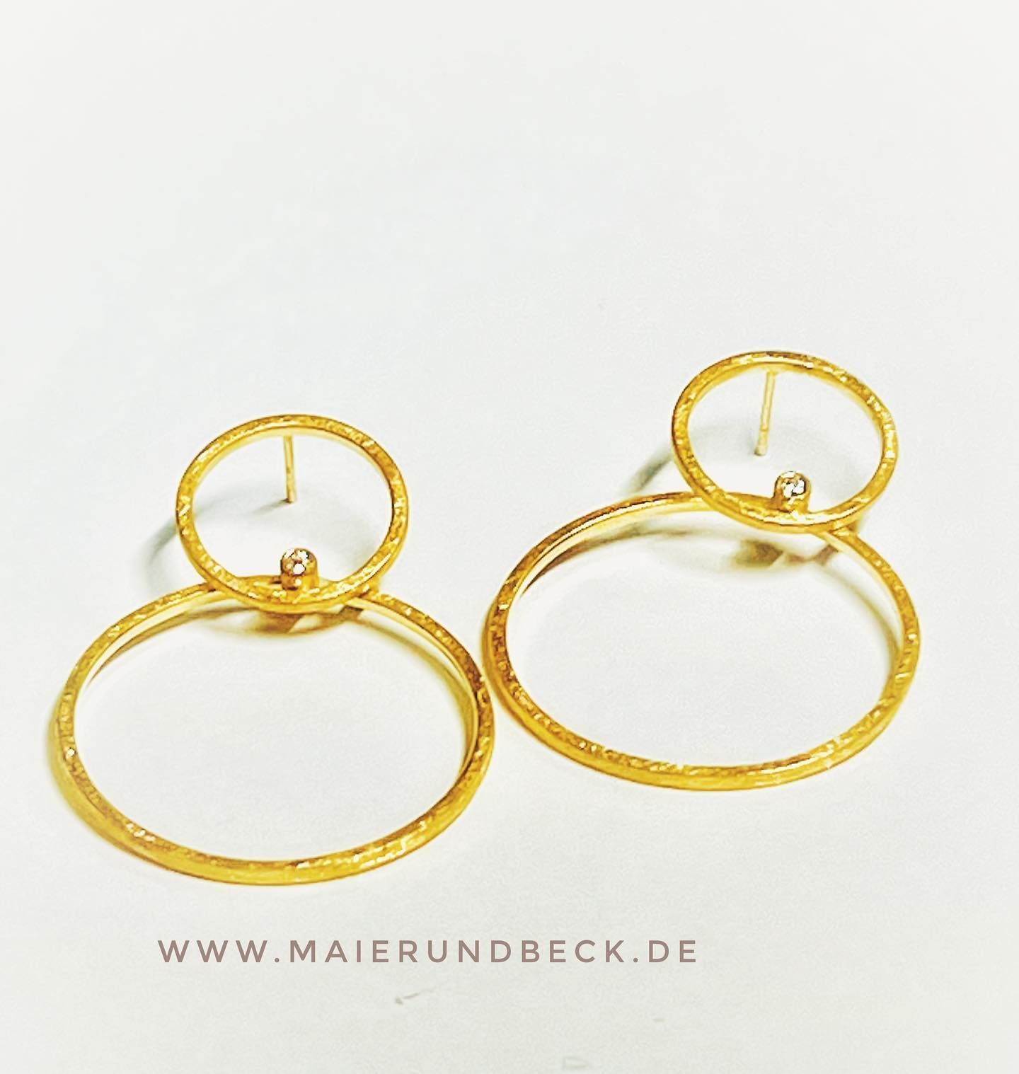 Gouden creolen met kleine diamantaccenten, rustend op een wit oppervlak.
