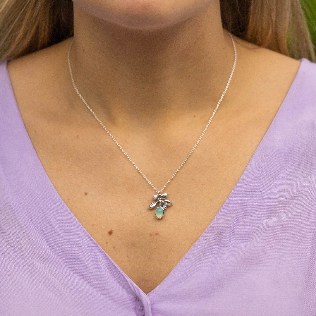 Vrouw draagt een zilveren ketting met een klein hangertje; lichtpaars shirt.