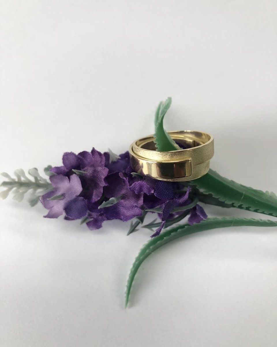 Gouden ring op een paarse kunstbloem tegen een witte achtergrond.