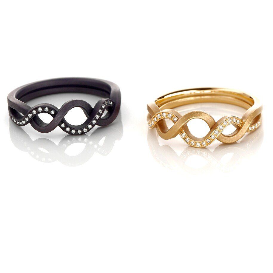 Twee ringen: een zwarte en een gouden, met oneindigheidsvormige ontwerpen en kleine diamanten.