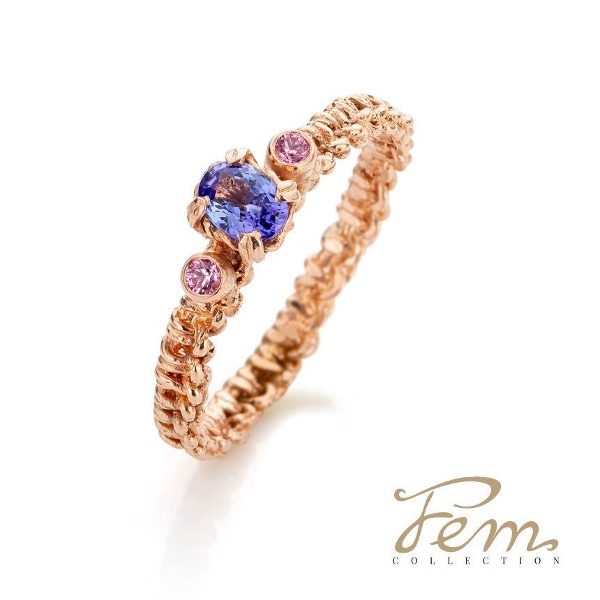 Roségouden ring met een blauwe en twee roze edelstenen. De ringband is getextureerd.