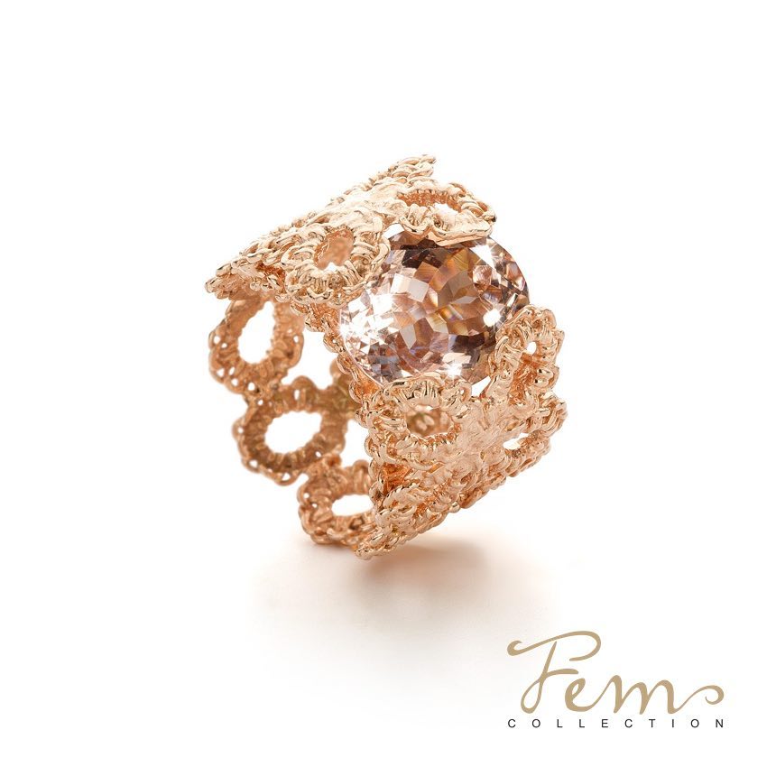 Roségouden ring met een grote, lichtbruine edelsteen, met een ingewikkeld kantpatroon op een witte achtergrond.