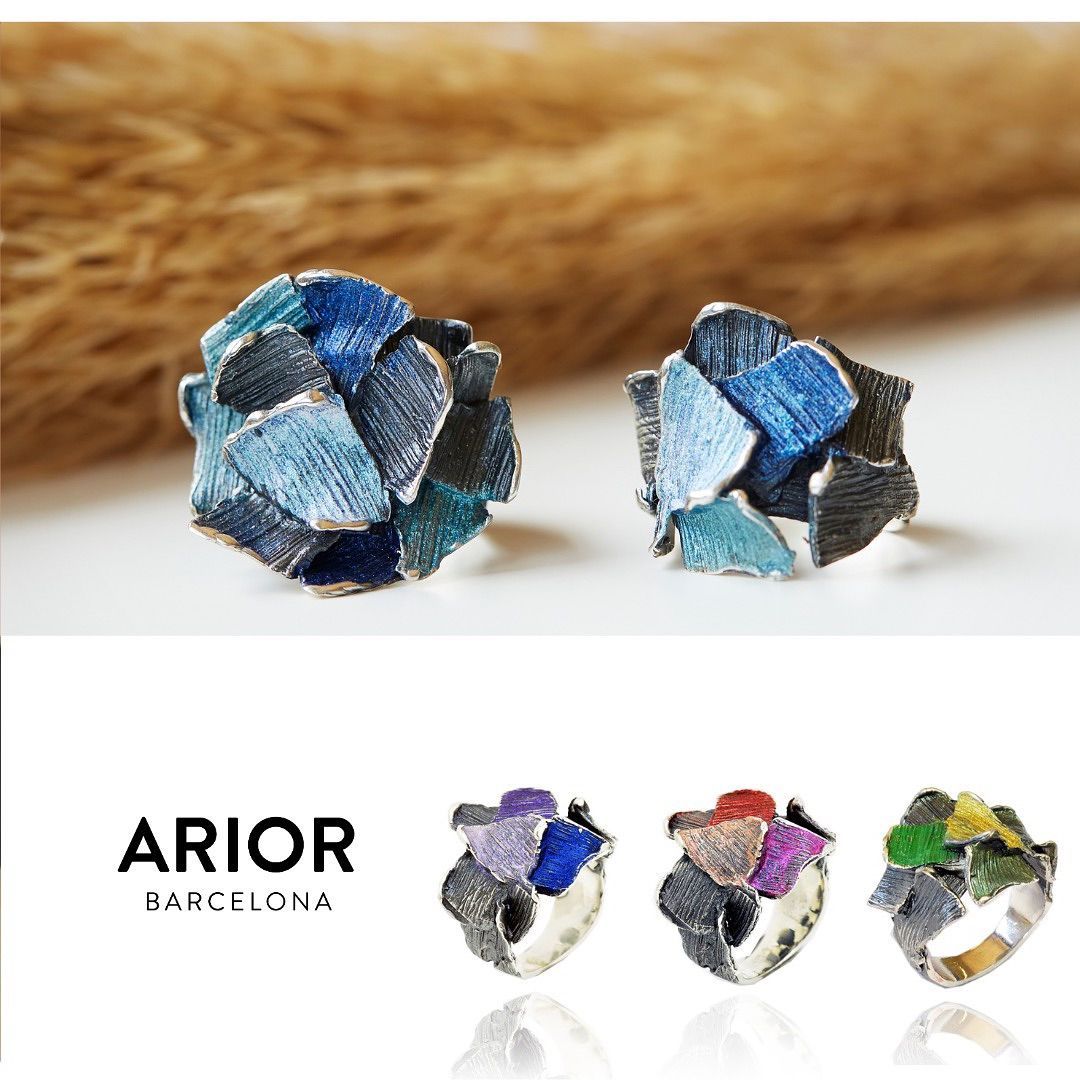 Twee zilveren ringen met abstracte, overlappende blauwe en zwarte emaille details, en drie andere gekleurde ringopties.