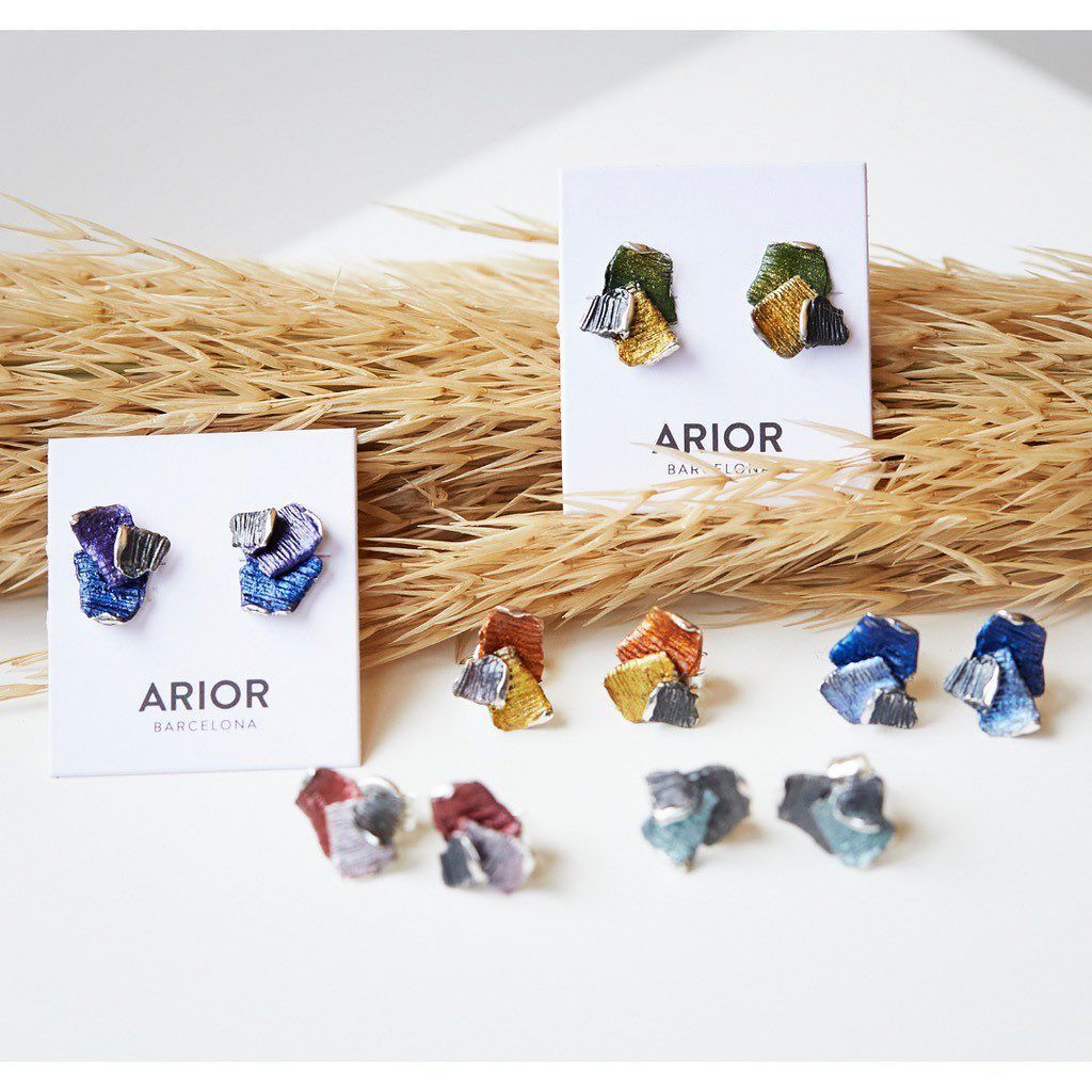 Oorbellen op displaykaartjes, met goud-, blauw- en groentinten. Gedroogd gras op de achtergrond.
