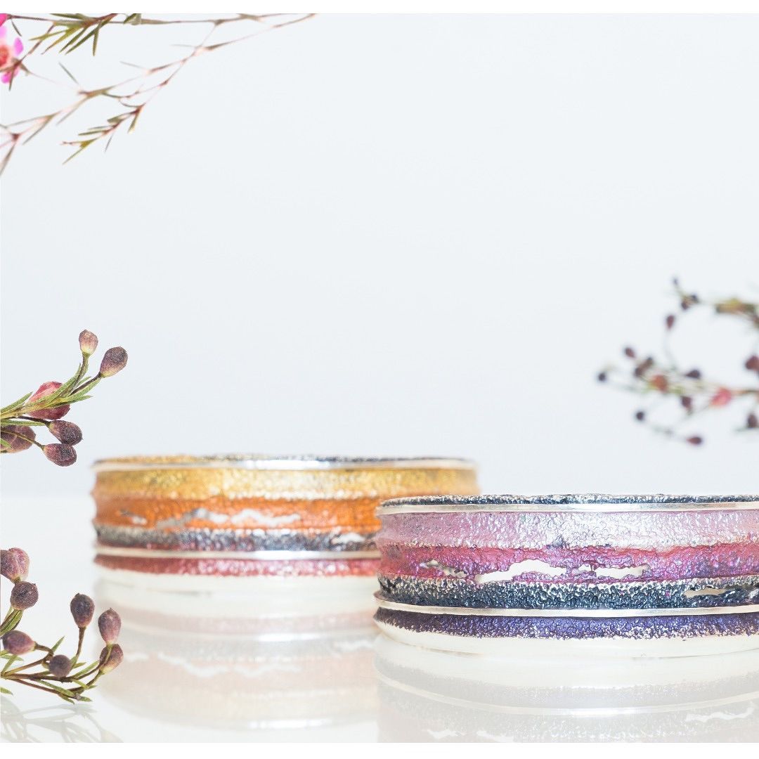 Twee decoratieve ringenhouders van glas met glinsterende banden; oranje en roze, met bloemenaccenten.