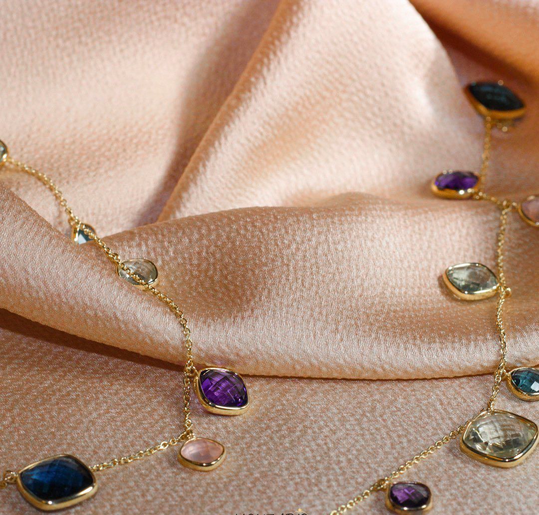 Gouden ketting met kleurrijke edelstenen op een roze satijnen stof.