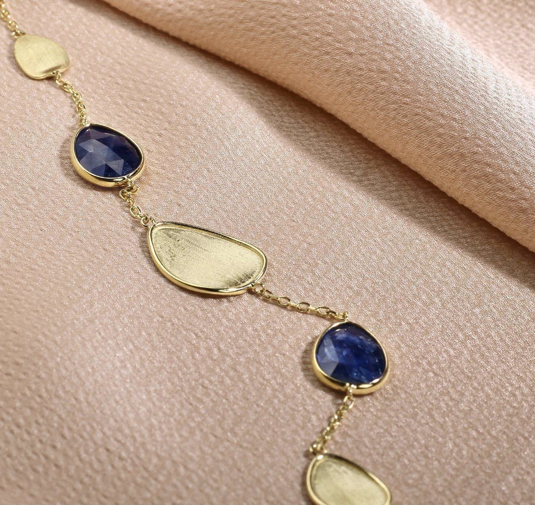 Gouden ketting met blauwe en gouden stenen op roze stof.