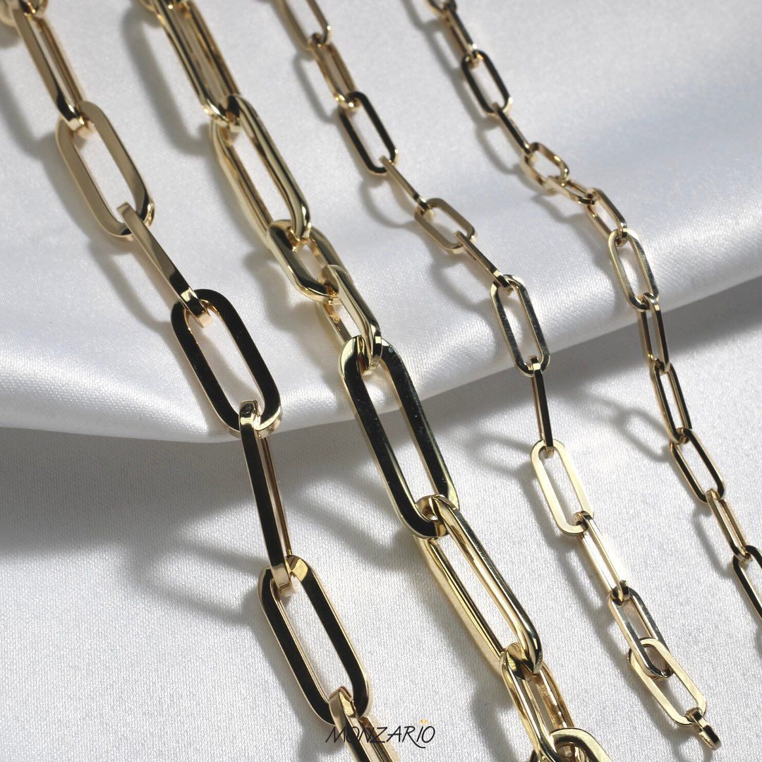 Gouden paperclipkettingen gedrapeerd op witte stof.