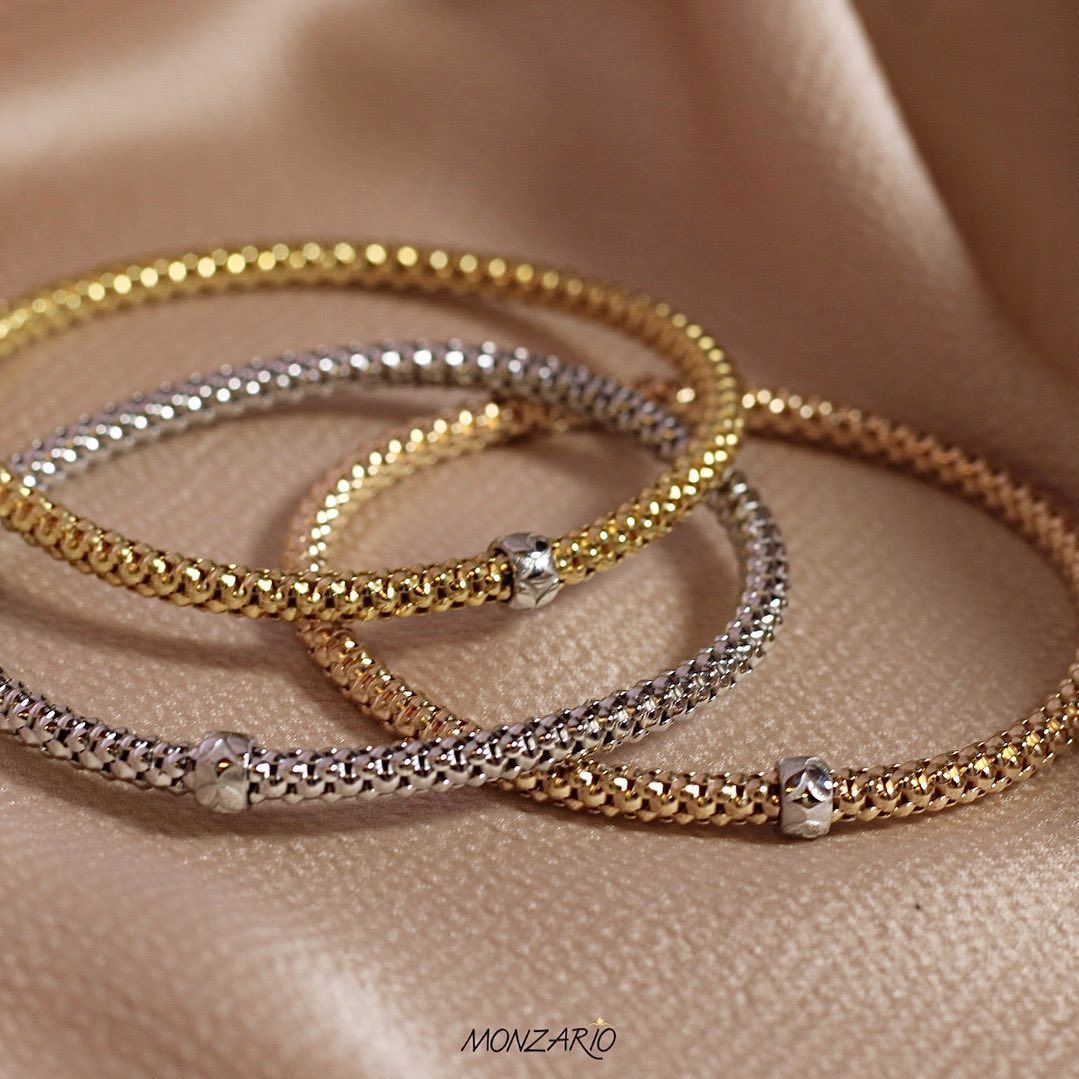 Drie armbanden met metalen kralen in goud en zilver, gelaagd op een beige stof.