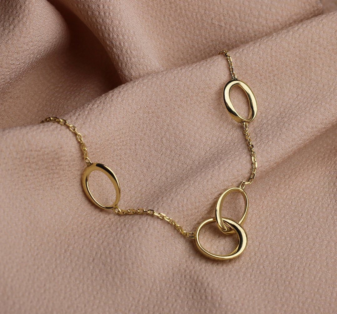 Gouden ketting met drie ovale schakels op een bruine stof.