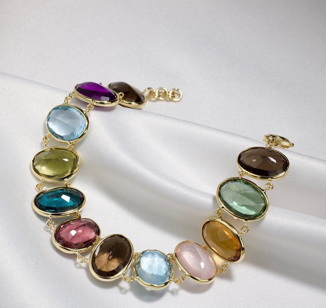 Gouden armband met ovale, veelkleurige edelstenen op wit satijn.