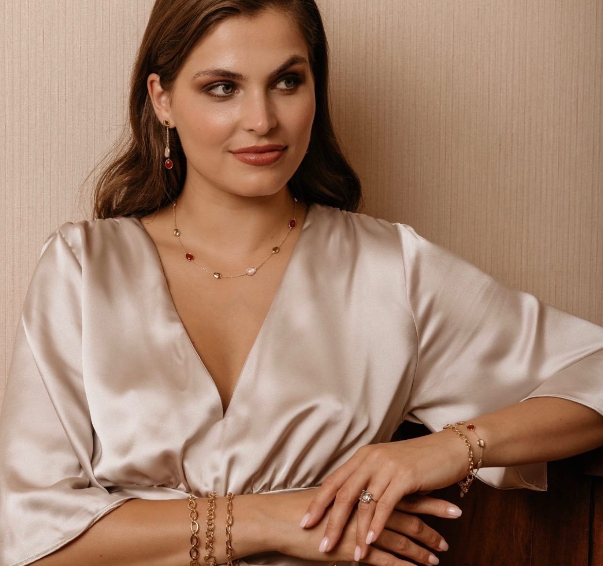 Vrouw met sieraden, zittend in een satijnen jurk. Sieraden: oorbellen, ketting, armbanden en een ring.