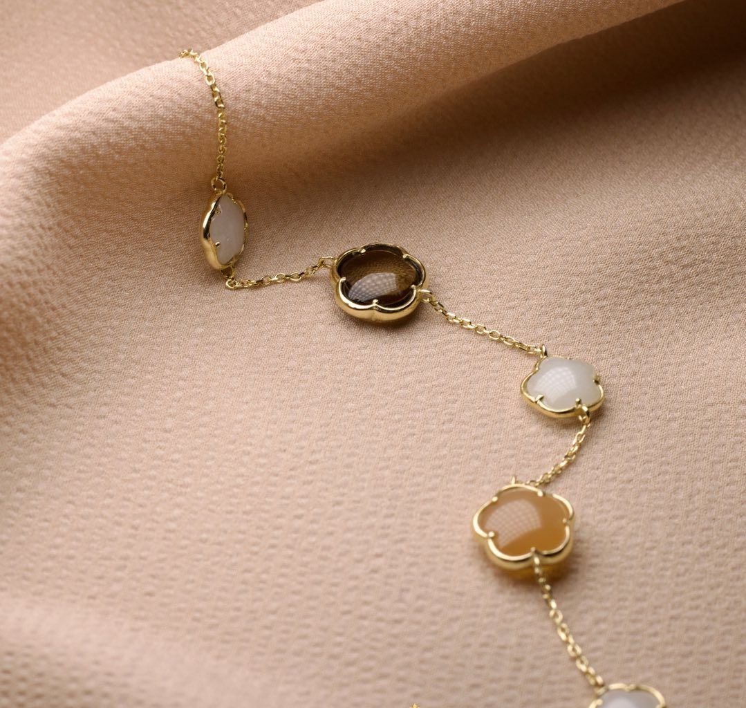 Gouden ketting met bloemvormige hangers, op beige stof.