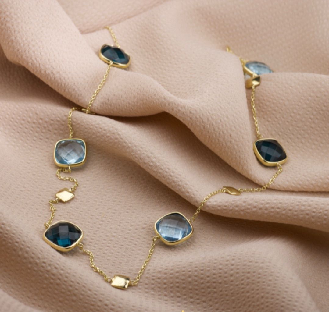 Gouden ketting met blauwe edelstenen op bruine stof.