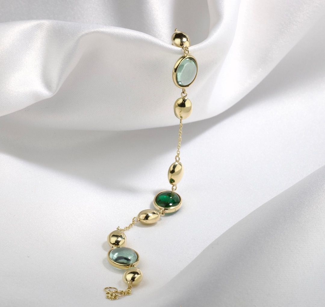 Gouden oorbelketting met groene en gouden stenen op een witte stoffen achtergrond.